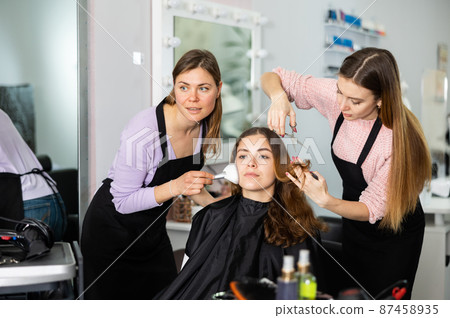 Make-up artist and a hairdresser serve a young female client 87458935