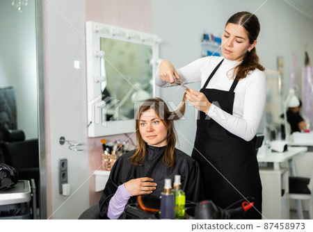 Female hairdresser cuts the hair of a young woman client 87458973