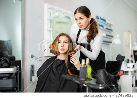 Young woman professional hair stylist choosing hairdo for female client Young woman professional hair stylist choosing hairdo for female client 87459022