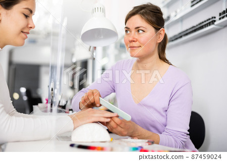 Skilled woman manicure master shaping nails to female client Skilled woman manicure master shaping nails to female client 87459024