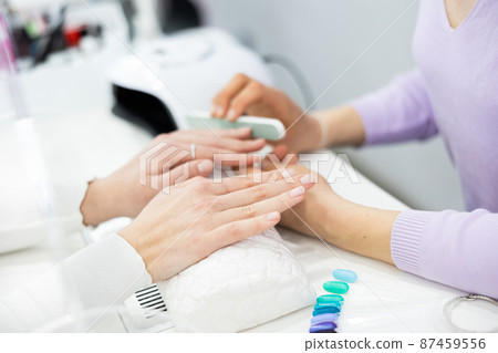 Cropped shot of woman manicurist filing and shaping nails of client Cropped shot of woman manicurist filing and shaping nails of client 87459556