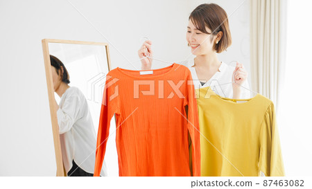 Fashion image of a young woman choosing clothes in front of a mirror Fashion image of a young woman choosing clothes in front of a mirror 87463082