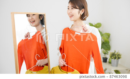 Fashion image of a young woman choosing clothes in front of a mirror 87463098