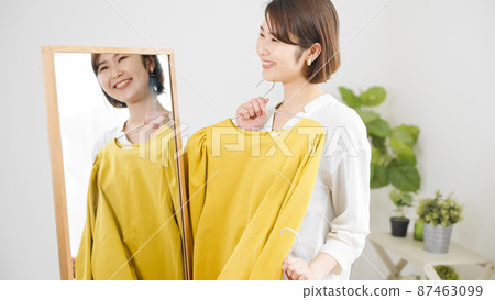 Fashion image of a young woman choosing clothes in front of a mirror 87463099