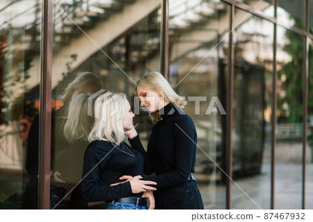 Two young females walking smiling embracing and kissing outdoor in the city 87467932