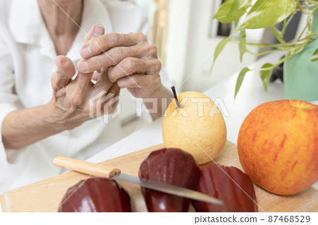 Close up of hands,old elderly cut her finger with a knife while slicing fruit in kitchen,senior woman pinching her index finger,pressing the wound to stop the bleeding at forefinger,first aid concept 87468529
