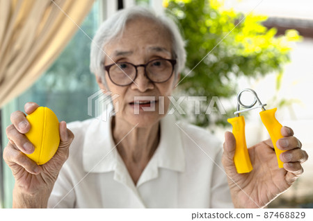 Asian senior woman doing hand,finger and wrist exercise with rubber ball and spring hand grip,stretch finger or squeeze with hand expander,physical therapy or recovery after injury,health care concept Asian senior woman doing hand,finger and wrist exercise with rubber ball and spring hand grip,stretch finger or squeeze with hand expander,physical therapy or recovery after injury,health care concept 87468829