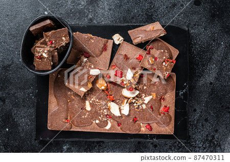 Craft homemade chocolate bars chopped on marble board. Black background. Top view Craft homemade chocolate bars chopped on marble board. Black background. Top view 87470311