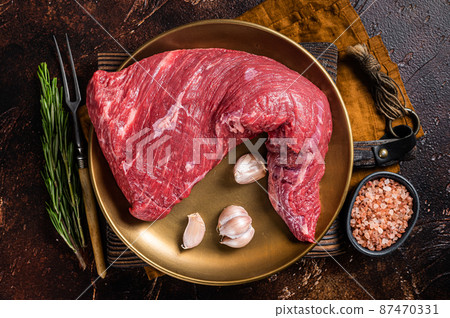 Raw tri-tip triangle roast or bottom sirloin steak on plate with herbs. Dark background. Top view Raw tri-tip triangle roast or bottom sirloin steak on plate with herbs. Dark background. Top view 87470331