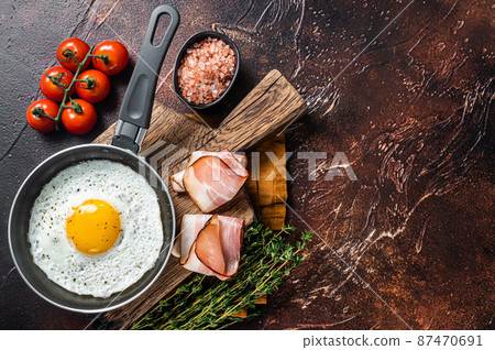 Fried egg in a frying pan with tomatoes and bacon. Black background. Top view. Copy space Fried egg in a frying pan with tomatoes and bacon. Black background. Top view. Copy space 87470691
