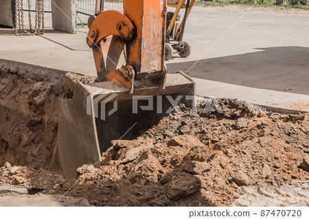 Excavation works. Tractor bucket digging with a heavy shovel on the ground at the construction site Excavation works. Tractor bucket digging with a heavy shovel on the ground at the construction site 87470720