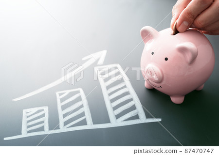 為未來系統地存錢的形象。把硬幣放在存錢罐裡。黑板上繪製的圖形和箭頭。 87470747