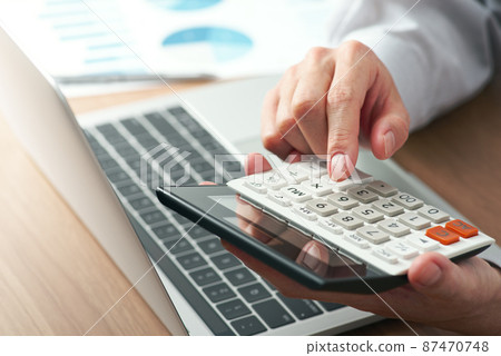 舉手用計算器計算。筆記本電腦和桌子上的報告。金融和計算的形象。 87470748