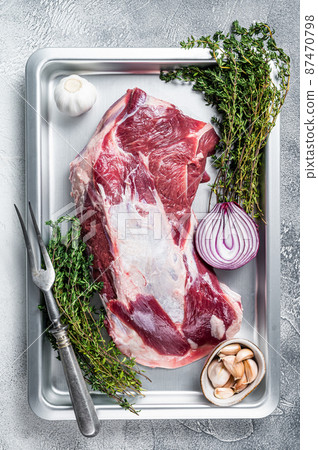 Raw lamb or goat shoulder meat in a baking dish with knife and meat fork. White background. Top view Raw lamb or goat shoulder meat in a baking dish with knife and meat fork. White background. Top view 87470798