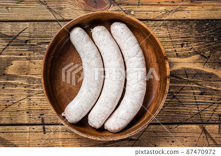 Raw Munich traditional white sausages in a wooden plate with herbs. wooden background. Top view 87470972