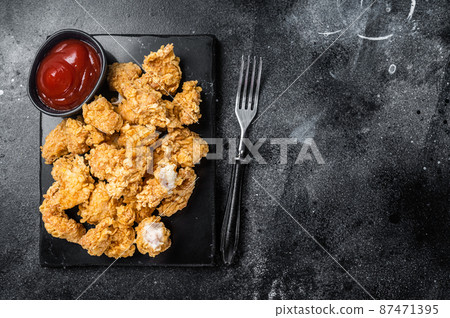 Crispy Fried breadcrumb covered chicken popcorn with ketchup. Black background. Top view. Copy space 87471395