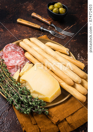 Appetizer plate with antipasti snacks grissini bread sticks, salami, olives and parmesan cheese. Dark bakground. Top view Appetizer plate with antipasti snacks grissini bread sticks, salami, olives and parmesan cheese. Dark bakground. Top view 87471403