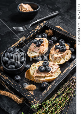 Foie gras toasts, duck liver pate and fresh blueberry in wooden tray. Black background. Top view Foie gras toasts, duck liver pate and fresh blueberry in wooden tray. Black background. Top view 87471475