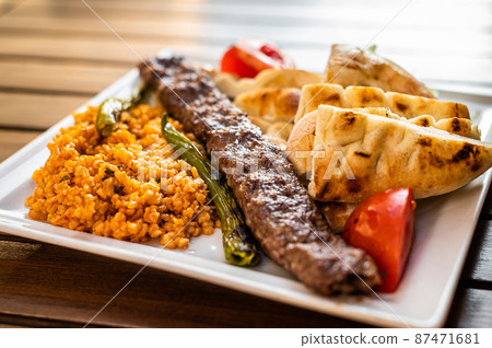 Turkish Adana kebab on a plate with marinated peppers, bread and rice pilaf. Top view 87471681