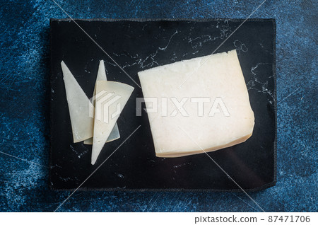 Hard goat cheese on marble board. Blue background. Top view 87471706