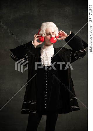 Portrait of young man wearing wig and vintage medieval outfit like famous composer having fun isolated on dark green vintage background. Portrait of young man wearing wig and vintage medieval outfit like famous composer having fun isolated on dark green vintage background. 87471845