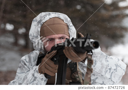 Soldier in winter camouflaged uniform in Modern warfare army on a snow day on forest battlefield with a rifle. Model face very similar to Ukraine prime minister. 87472726
