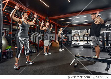 Young and active people on group sports training together do warming up and doing exercise for arm stretch. People train in spacious bright gym. Concept of sport and healthy lifestyle Young and active people on group sports training together do warming up and doing exercise for arm stretch. People train in spacious bright gym. Concept of sport and healthy lifestyle 87477187