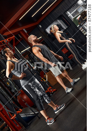 Young and active people on group sports training together do warming up and doing exercise for arm stretch. People train in spacious bright gym. Concept of sport and healthy lifestyle Young and active people on group sports training together do warming up and doing exercise for arm stretch. People train in spacious bright gym. Concept of sport and healthy lifestyle 87477188