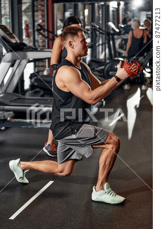 A man trains his arms and chest in the gym on the simulator, does exercises for different muscle groups. Fintes motivation, sports lifestyle, health, athletic body, body positive. Film grain. 87477213