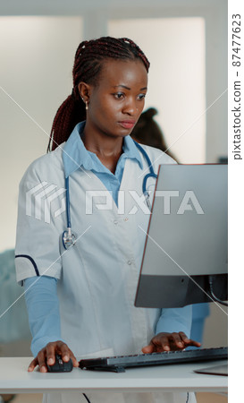General practitioner with white coat using computer at desk General practitioner with white coat using computer at desk 87477623