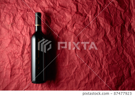 Bottle of red wine on a crumpled red paper background. 87477923