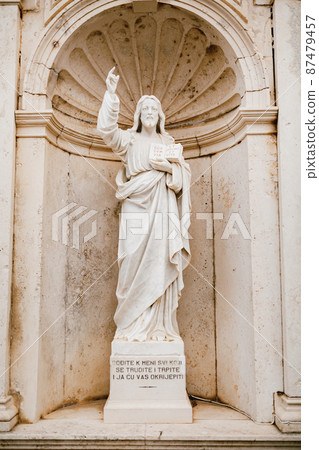 Statue of Jesus Christ with a book in hands near the Church of the Nativity of the Virgin in Prcanj 87479457