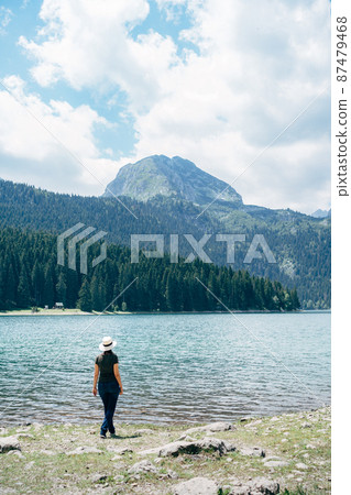 Woman stands on the shore of the bay and looks at the mountains. Back view Woman stands on the shore of the bay and looks at the mountains. Back view 87479468