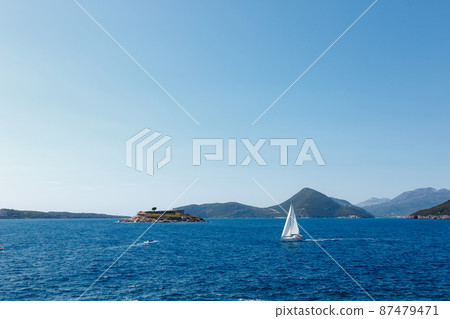 Sailboat sails past the coast of Montenegro to the Mamula island Sailboat sails past the coast of Montenegro to the Mamula island 87479471