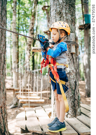 Boy stands on a wooden platform and looks at the safety belt 87479598