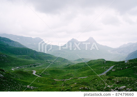 Asphalt road in a valley with mountains in the fog in the background in Durmitor National Park 87479660