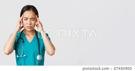 Healthcare workers, preventing virus, quarantine campaign concept. Close-up of overworked and tired asian doctor, nurse having headache, looking troubled, standing white background Healthcare workers, preventing virus, quarantine campaign concept. Close-up of overworked and tired asian doctor, nurse having headache, looking troubled, standing white background 87480900