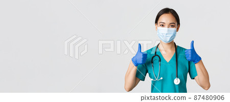 Covid-19, coronavirus disease, healthcare workers concept. Confident smiling asian doctor, nurse in medical mask and rubber gloves, show thumbs-up in approval, provide service, wite background 87480906