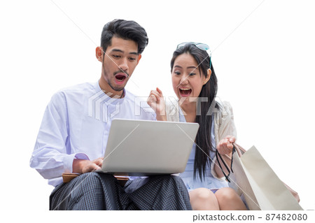 Young man and asian woman sit playing laptop with excited and shocked, isolated on background Young man and asian woman sit playing laptop with excited and shocked, isolated on background 87482080