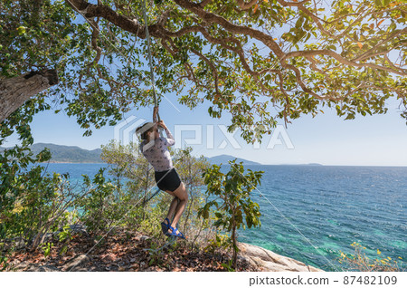 Young woman hanging rope with tree in tropical sea 87482109