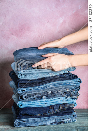 Woman folding stylish jeans on wooden table, closeup 87482279