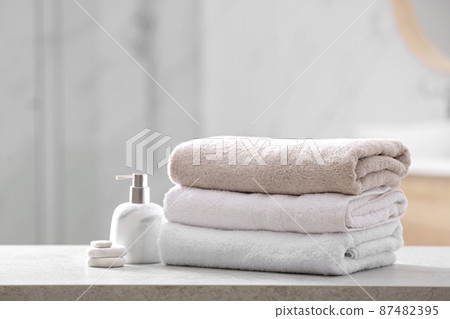 Clean towels, spa stones and soap dispenser on table in bathroom Clean towels, spa stones and soap dispenser on table in bathroom 87482395