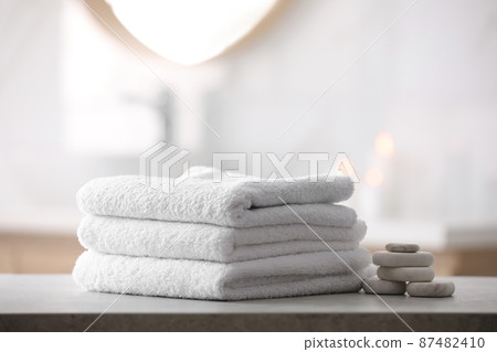Stack of fresh towels and spa stones on table in bathroom Stack of fresh towels and spa stones on table in bathroom 87482410