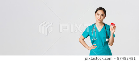 Healthcare workers, preventing virus, quarantine campaign concept. Skeptical and displeased asian female physician, nurse do not recommend medication, smirk reluctant and show pills, white background 87482481