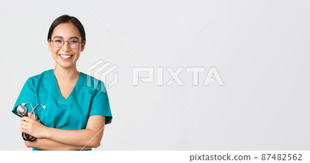 Covid-19, coronavirus disease, healthcare workers concept. Confident happy asian female physician, doctor in glasses, cross arms chest and smiling, holding stethoscope for examination Covid-19, coronavirus disease, healthcare workers concept. Confident happy asian female physician, doctor in glasses, cross arms chest and smiling, holding stethoscope for examination 87482562