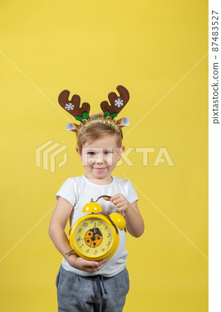 A smiling little boy in in christmas reindeer costume with alarm clock 87483527