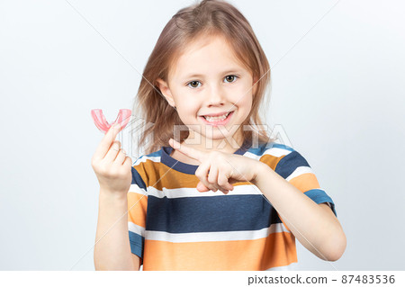 Cute little girl with blond hair is holding a pink dental myofunctional trainer Cute little girl with blond hair is holding a pink dental myofunctional trainer 87483536
