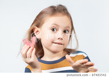 Cute little girl with blond hair is holding a pink dental myofunctional trainer Cute little girl with blond hair is holding a pink dental myofunctional trainer 87483542