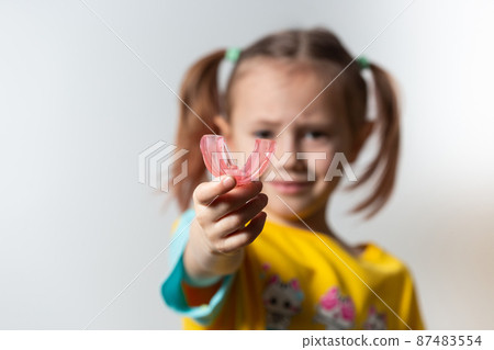 Cute little girl with blond hair is holding a pink dental myofunctional trainer Cute little girl with blond hair is holding a pink dental myofunctional trainer 87483554