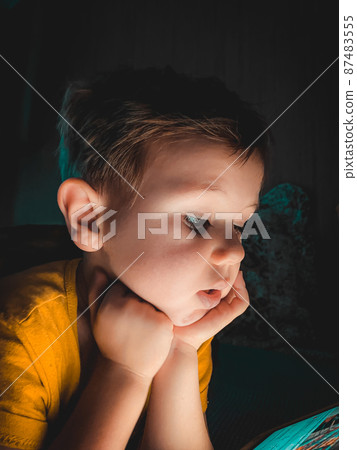 Little boy looking at a tablet in the evening in the dark on the bed Little boy looking at a tablet in the evening in the dark on the bed 87483555